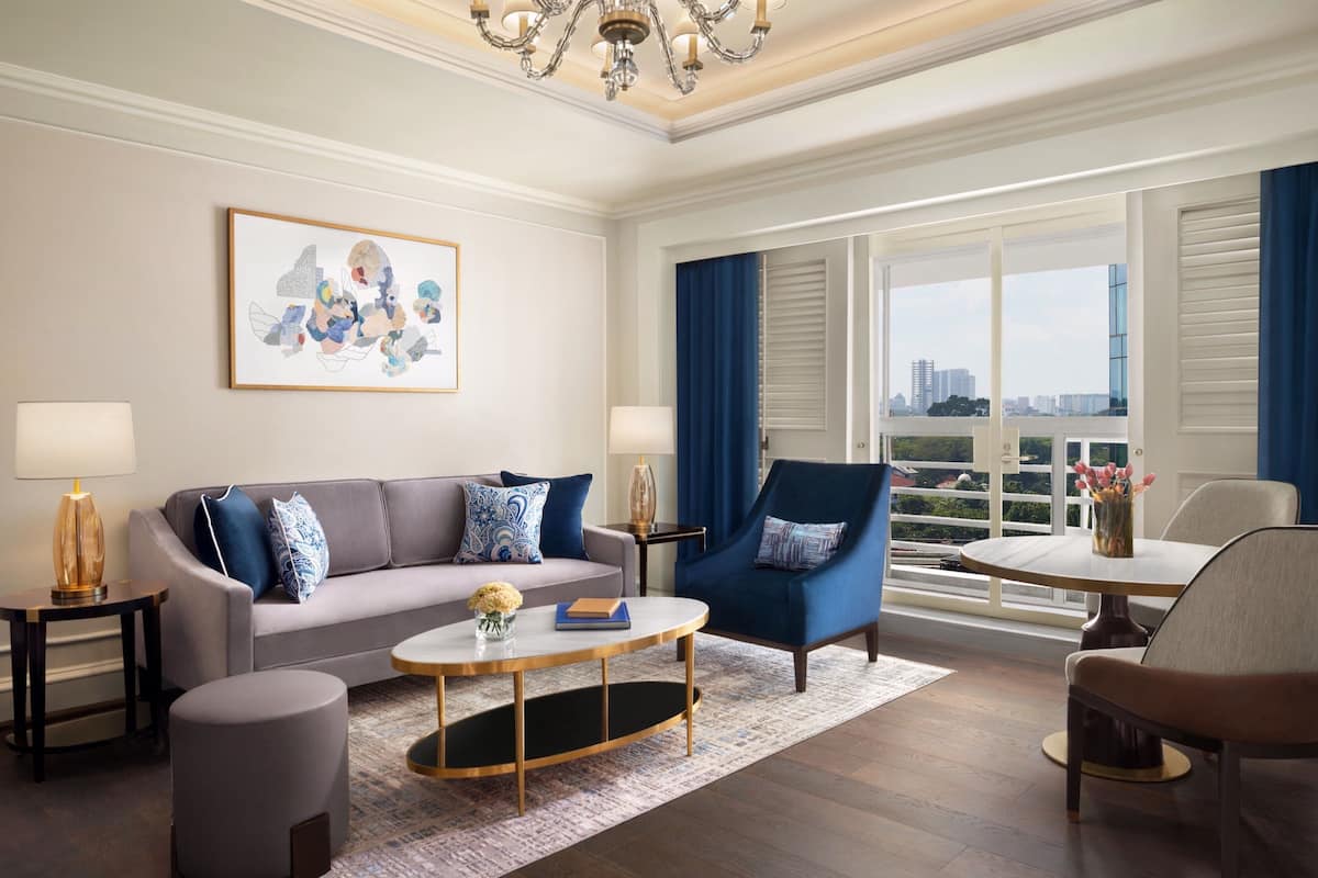 A modern living room with a sofa, armchair, coffee table, and a view of the city through large windows.
