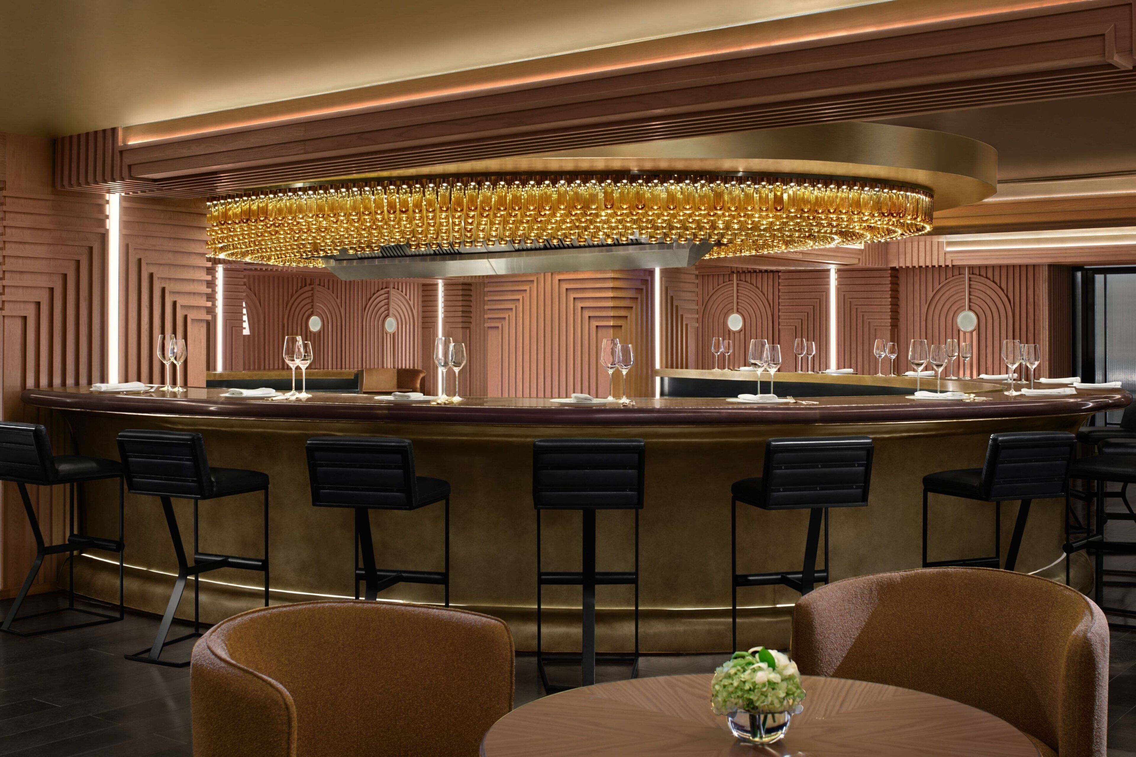 A bar area with a circular bar, multiple stools, and a round table with a vase of flowers.