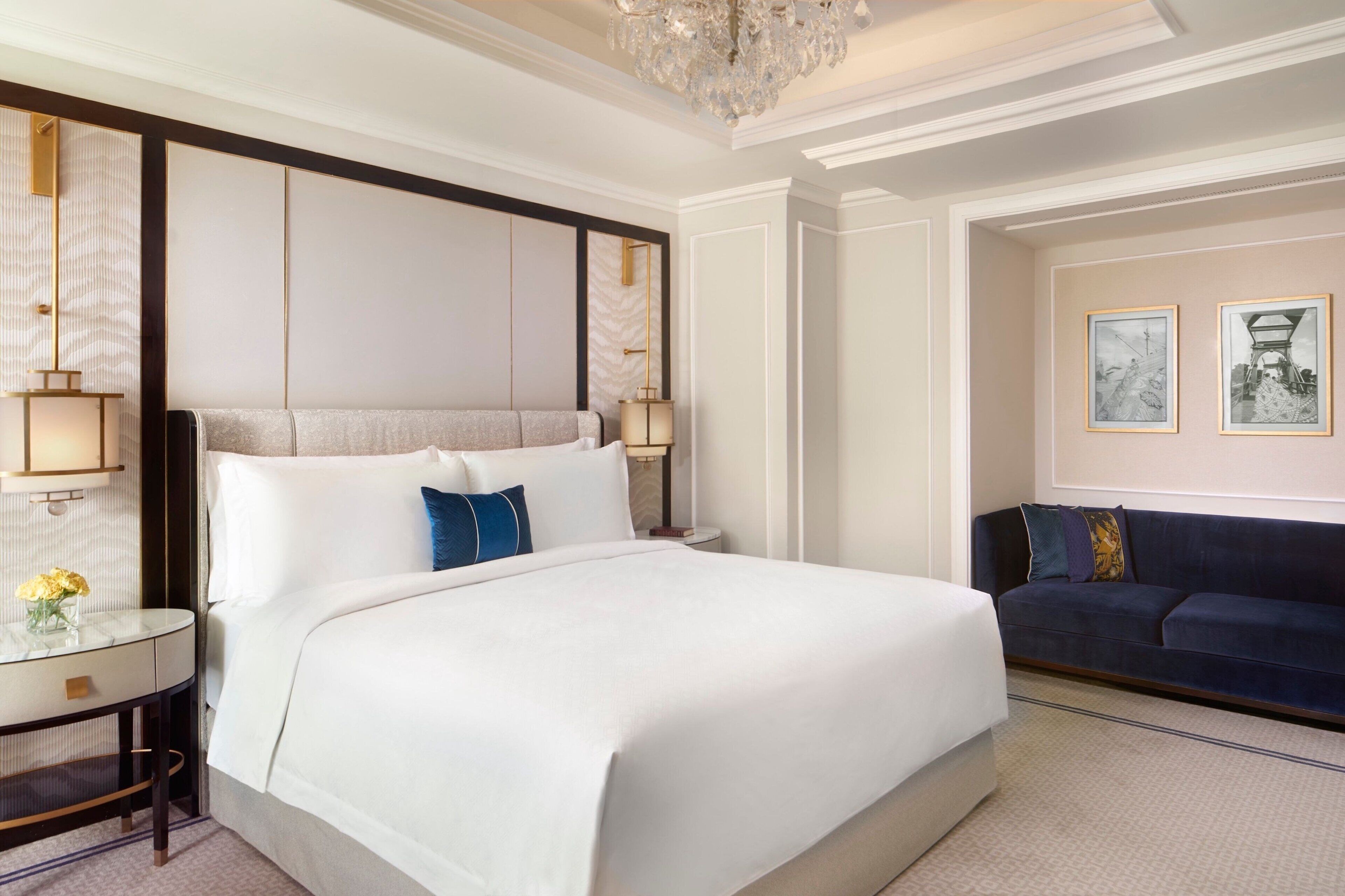 A hotel room with a large bed, a dark blue sofa, a small table with a vase of flowers, and two framed pictures on the wall.