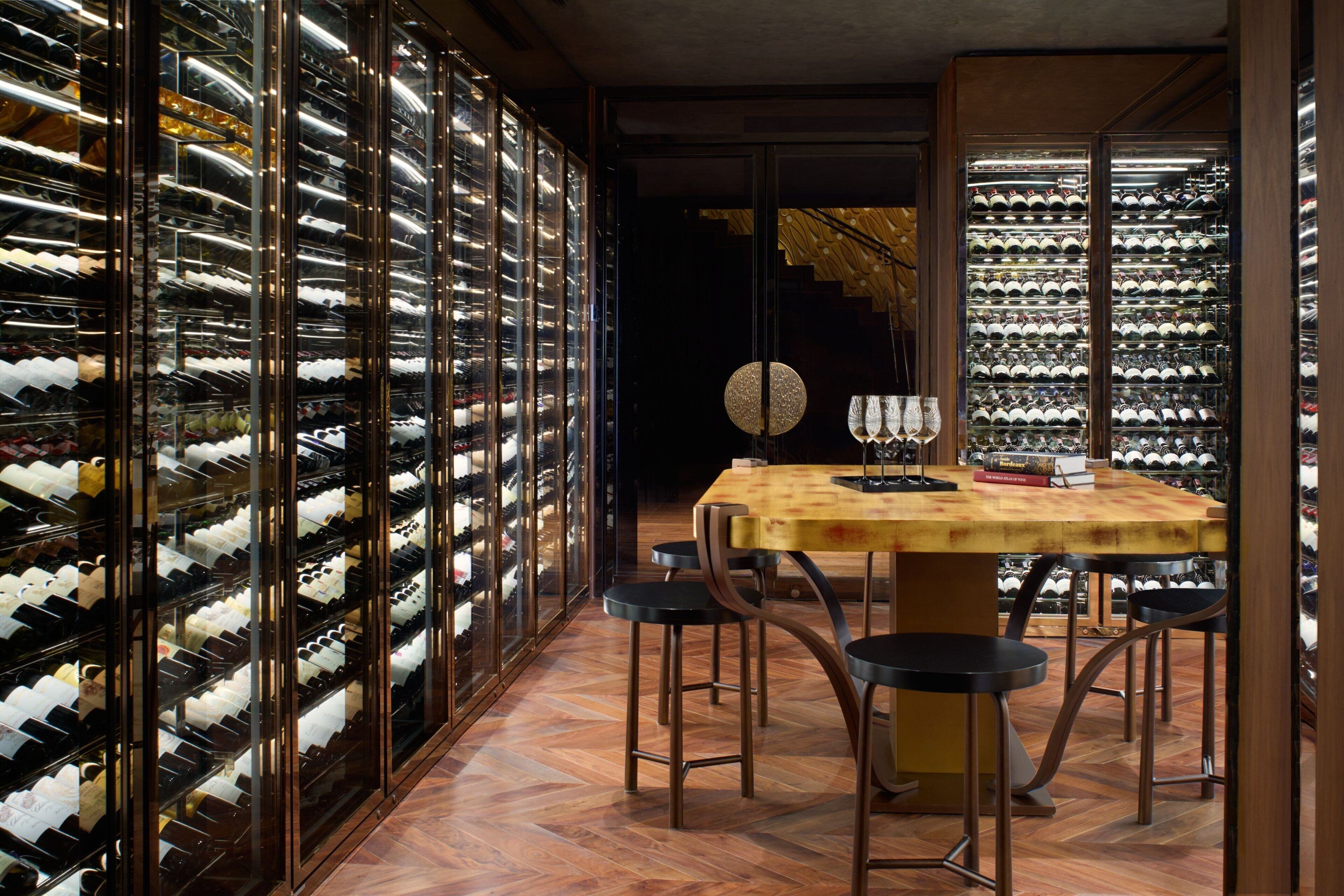 A wine cellar with multiple wine racks, a wooden table, and bar stools.