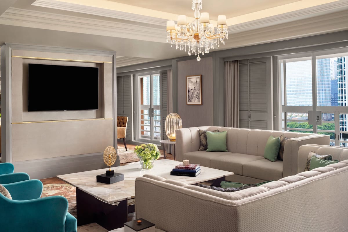 A modern living room with a large flat-screen TV, a chandelier, and a sofa with green cushions.