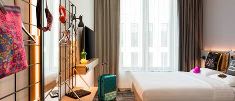 A hotel room with a bed, a desk, a chair, a suitcase, and a window with curtains.