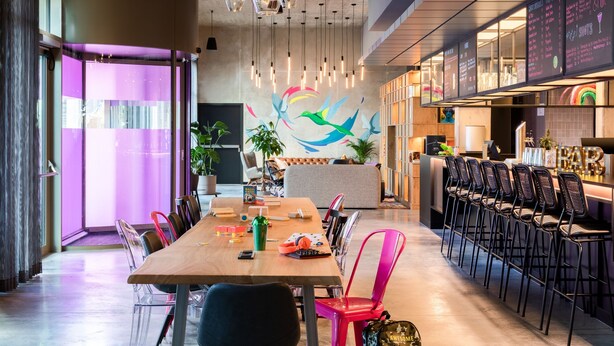 Un comedor moderno con una larga mesa de madera, sillas coloridas y una barra con taburetes altos.