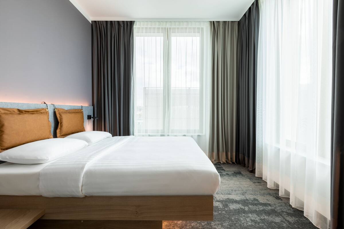 Habitació d'hotel amb un llit, un capçal i una finestra amb cortines.
