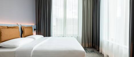 A hotel room with a bed, a headboard, and a window with curtains.