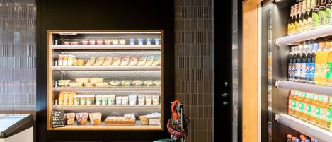 A vending machine with various food and drink options, a blue suitcase, and a wooden panel wall.