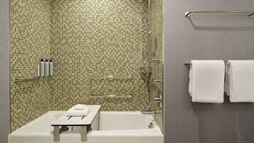 A modern bathroom with a mosaic tile shower wall, a white bathtub, and a towel rack with two towels.