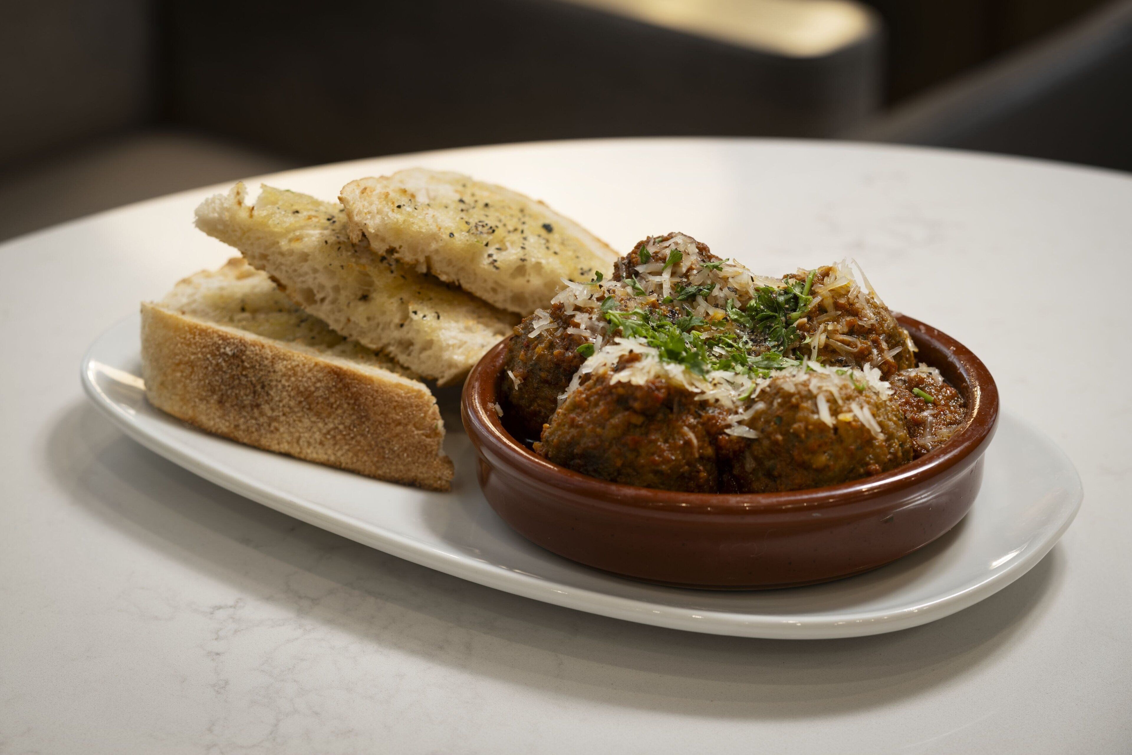 Un plato con albóndigas y queso rallado, acompañado de rebanadas de pan sobre una mesa blanca.