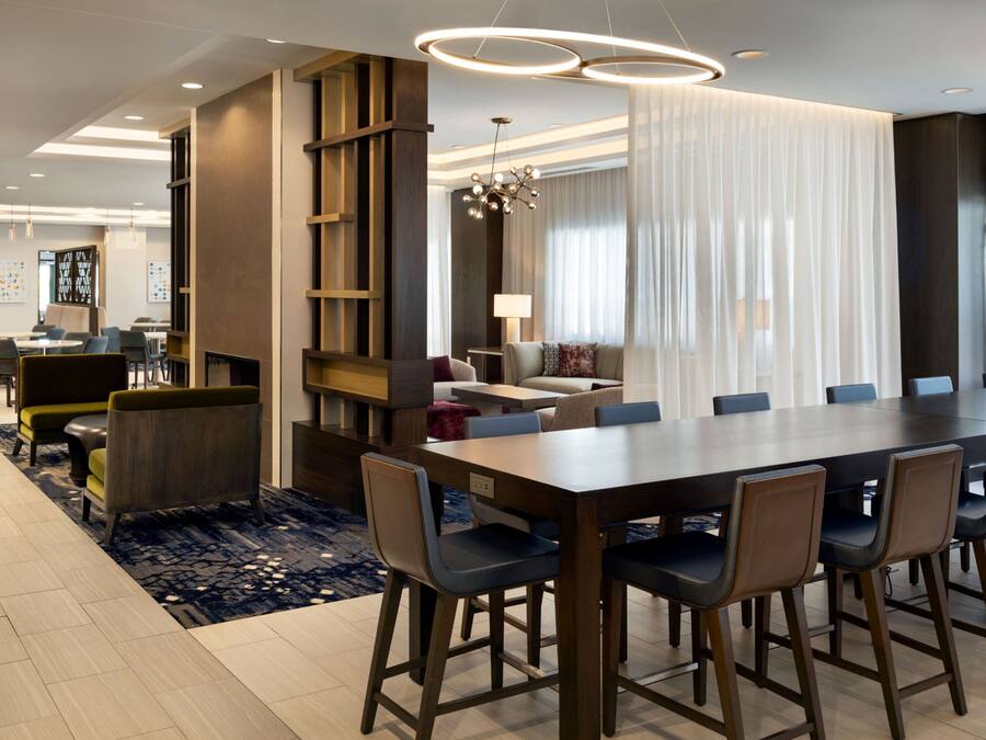 A modern dining area with a long table, multiple chairs, and a decorative chandelier.