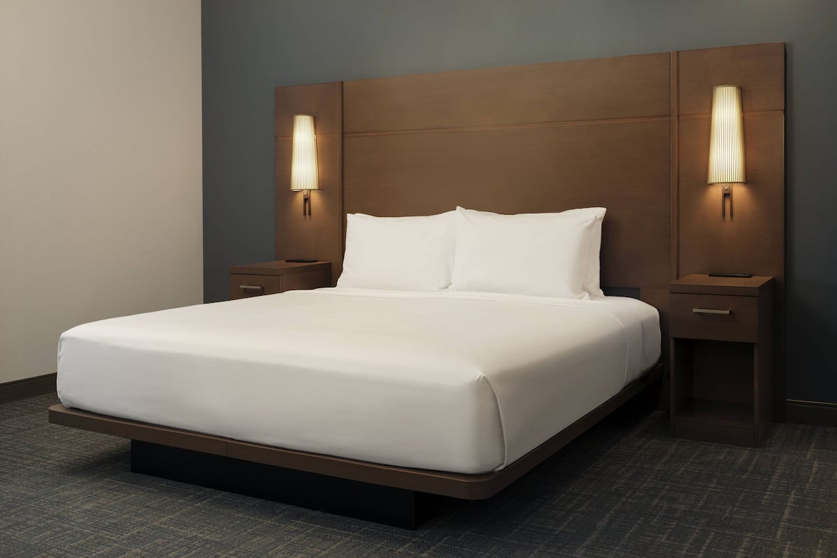 A hotel room with a large bed, two bedside tables, and wall-mounted lamps.