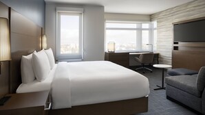 A hotel room with a large bed, a desk, a chair, a TV, and a view of the city. - Residence Inn by Marriott Oakland Downtown (Oakland)