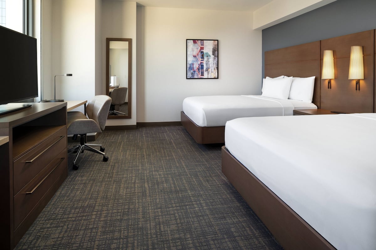 A hotel room with two beds, a desk with a computer, a chair, and a large window.