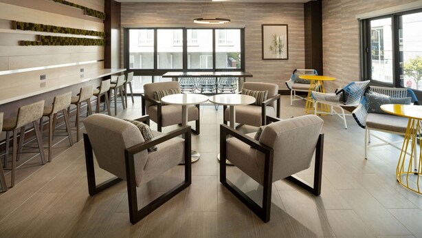 A modern interior with a central round table surrounded by chairs, a bar area with stools, and a seating area with a yellow table. - Residence Inn by Marriott Oakland Downtown (Oakland)