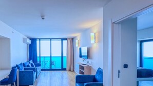 A modern hotel room with a balcony, a seating area with blue chairs, a flat-screen TV, and a wooden side table. - ORBI CITY Hotel Sea View (Batumi)