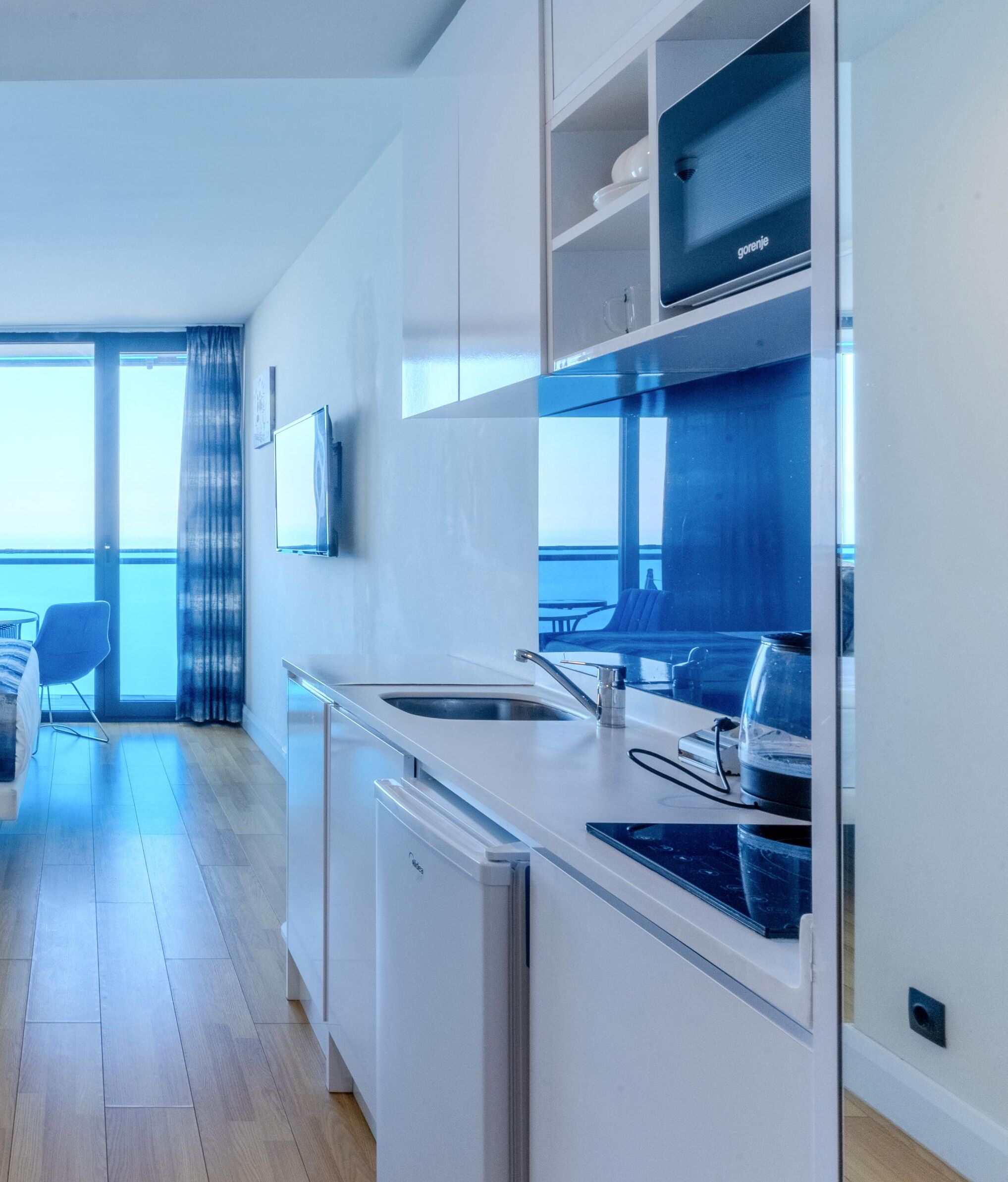 A modern kitchen with white cabinets, a built-in oven, and a large window overlooking a balcony.
