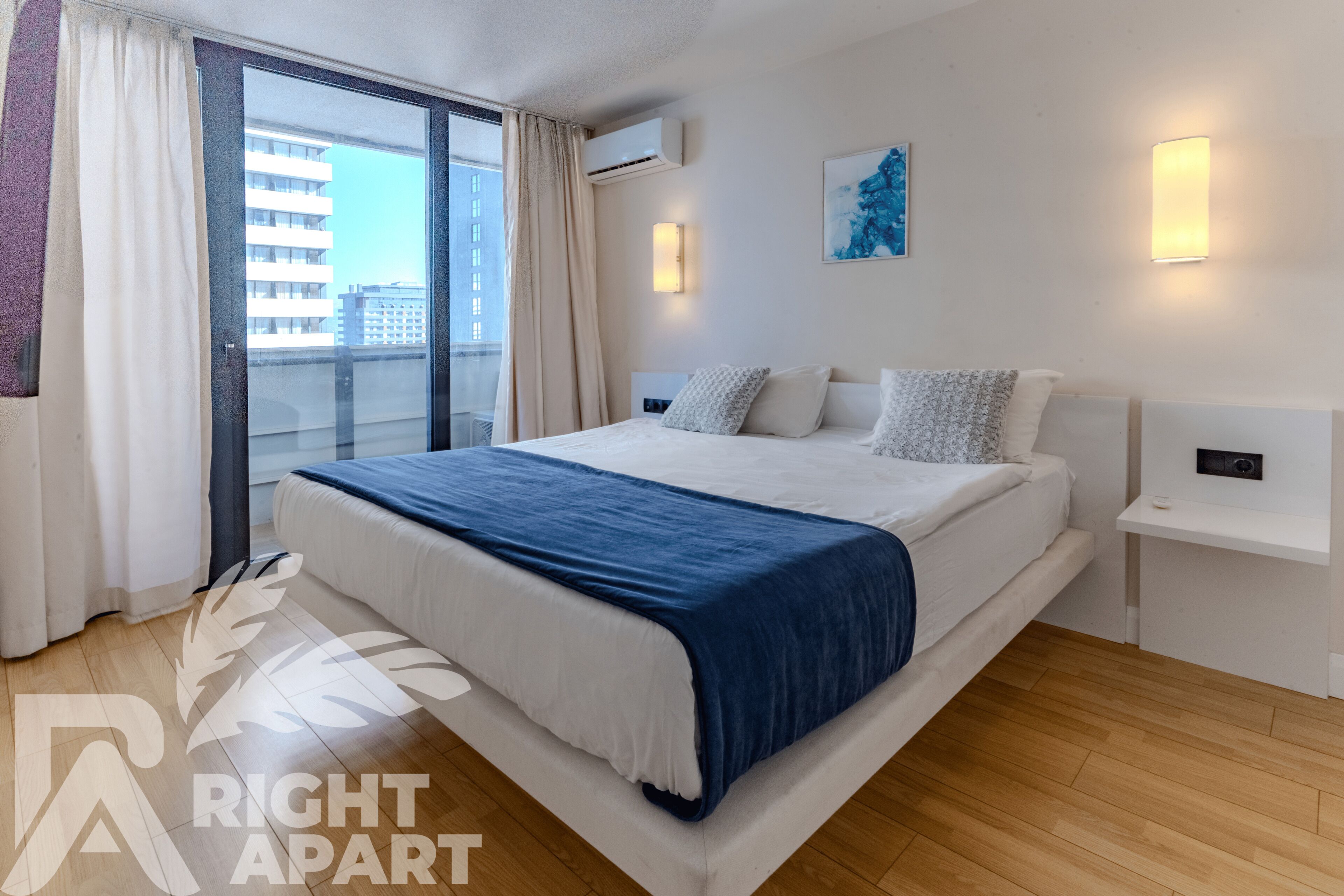 Une chambre d’hôtel moderne avec un grand lit, un balcon avec des rideaux, un climatiseur fixé au mur et un tableau.