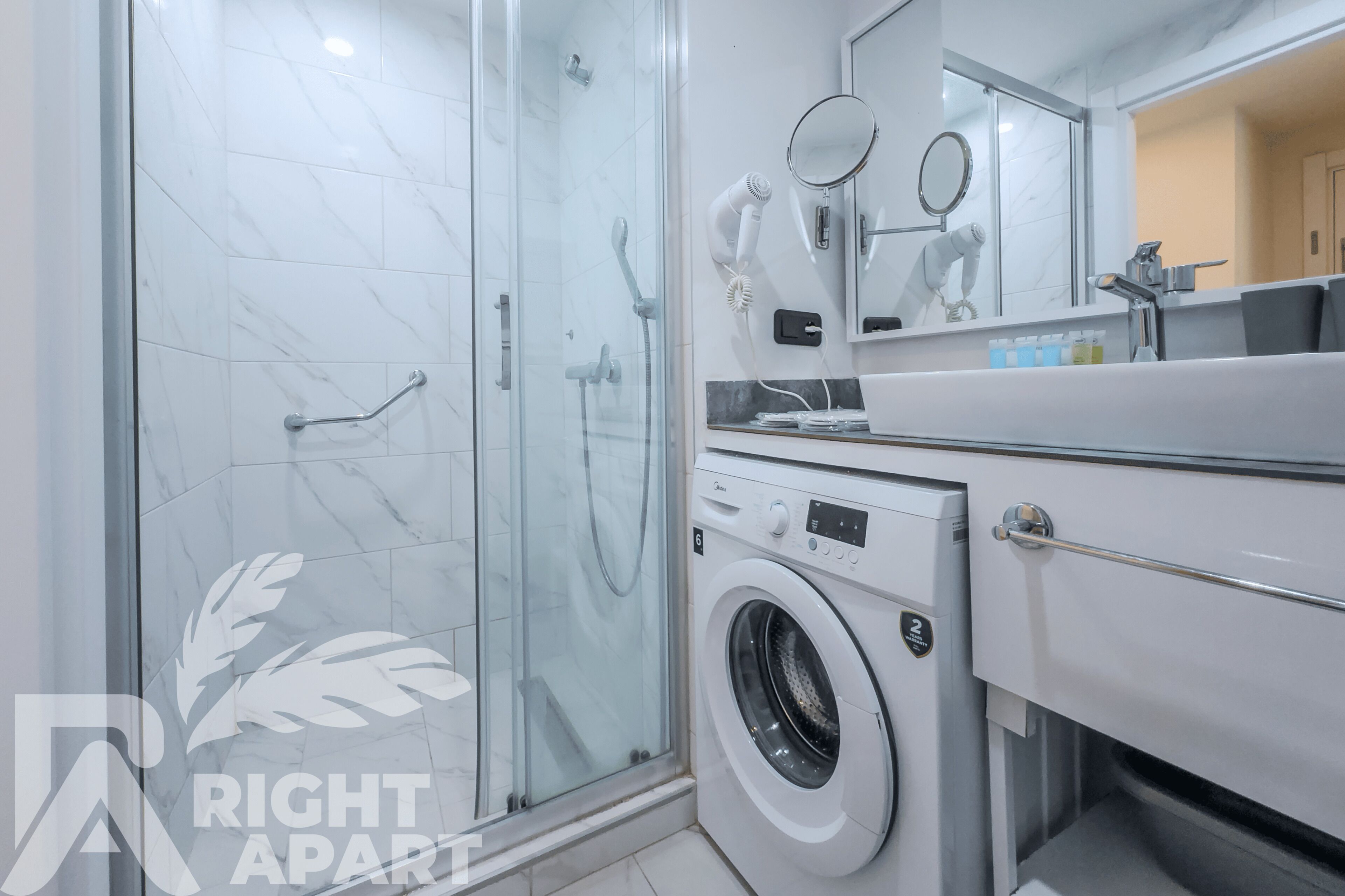 A modern bathroom with a glass-enclosed shower, a built-in washing machine, and a vanity with a mirror.