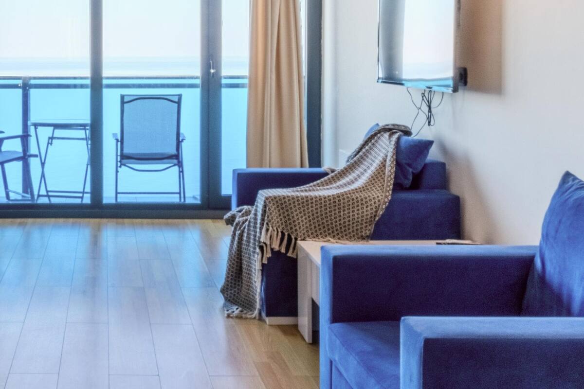 Ein modernes Wohnzimmer mit einer Couch, einem an der Wand montierten Fernseher und Meerblick durch große Fenster.