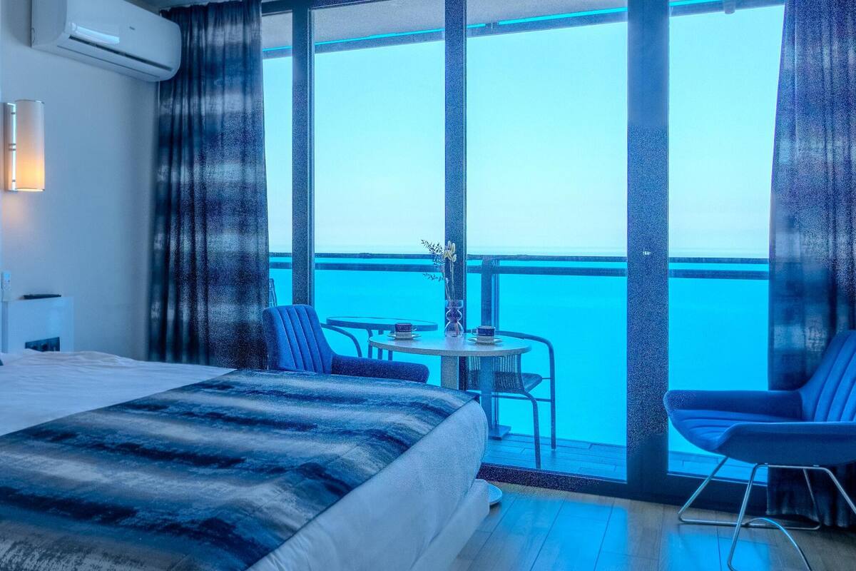 Ein Hotelzimmer mit einem großen Bett, einem kleinen Tisch mit Stühlen und einem Balkon mit Meerblick.