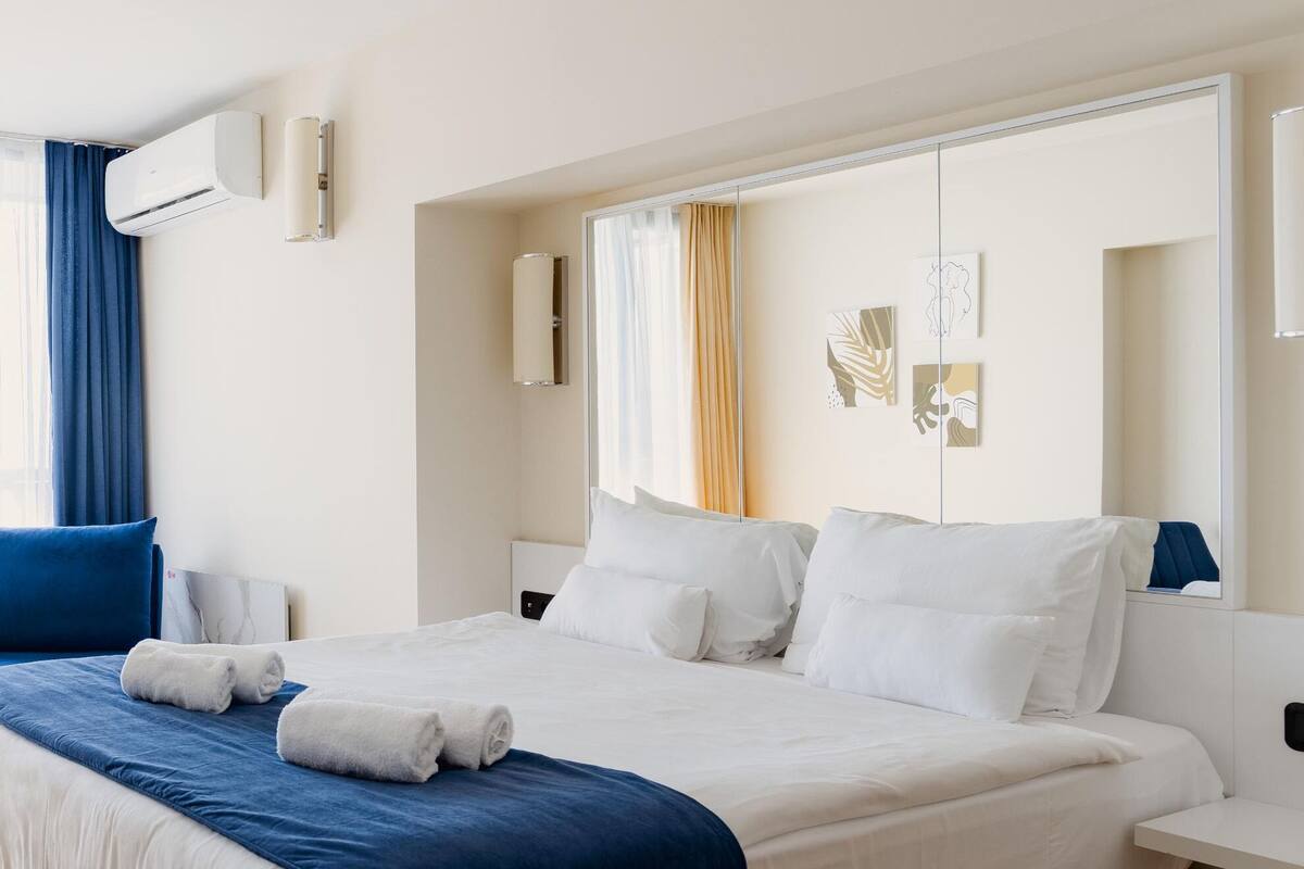 Ein modernes Hotelzimmer mit einem großen Bett, einem Nachttisch, einem Spiegel und einer Klimaanlage.