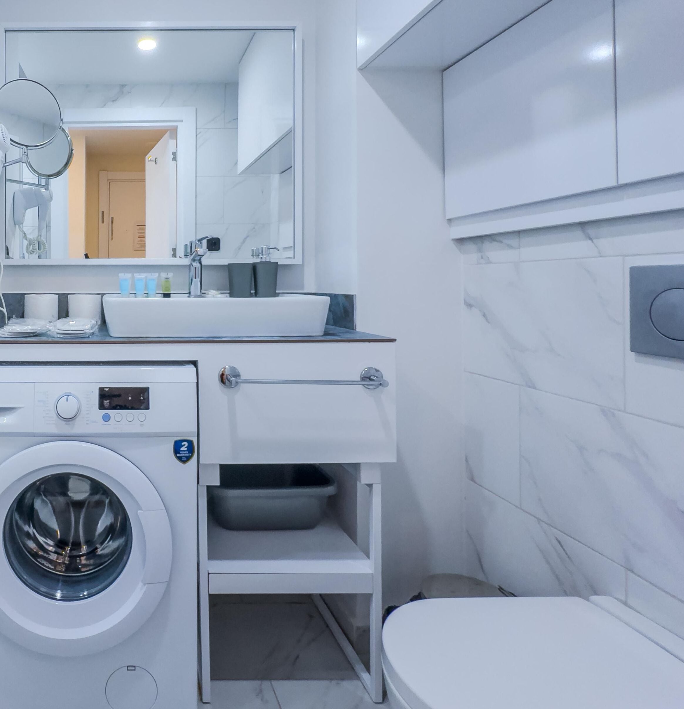 Un baño moderno con lavadora incorporada, un lavamanos con espejo arriba y un inodoro.