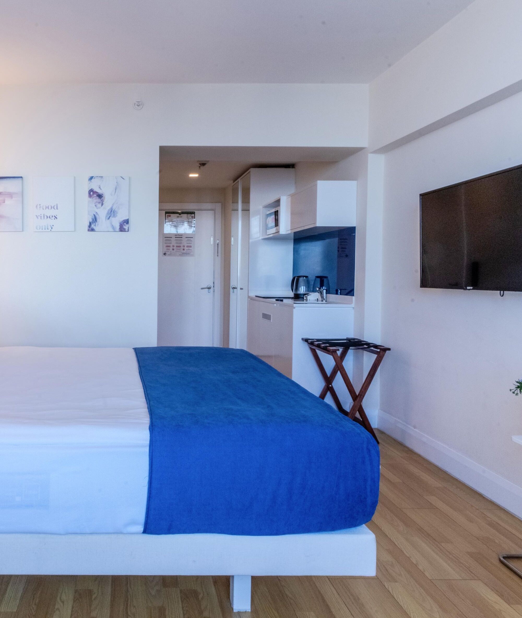 Een hotelkamer met een bed, een kleine keukenhoek en een aan de muur bevestigde televisie.
