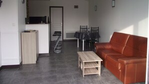 A living room with a brown leather sofa, a wooden coffee table, and a dining area with a table and chairs. - Countryside at the foot of Mont Saint Michel (Roz-sur-Couesnon)