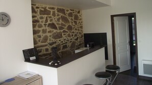 A kitchen with a stone wall, a clock, a bar counter, and a door leading to another room. - Countryside at the foot of Mont Saint Michel (Roz-sur-Couesnon)