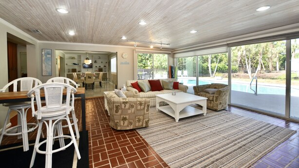 A spacious living area with a pool view, white wicker furniture, and a large window.