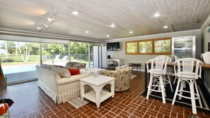 A spacious living area with a large window, a sofa, a coffee table, and two white bar stools.