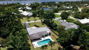 An aerial view of a residential area with a large swimming pool, surrounded by lush greenery and houses.