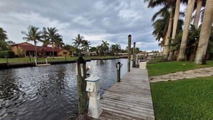 A wooden dock extending into a calm water body, surrounded by lush greenery and palm trees.