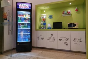 Una máquina expendedora con diversas bebidas, un microondas y una encimera verde con un estante superior.