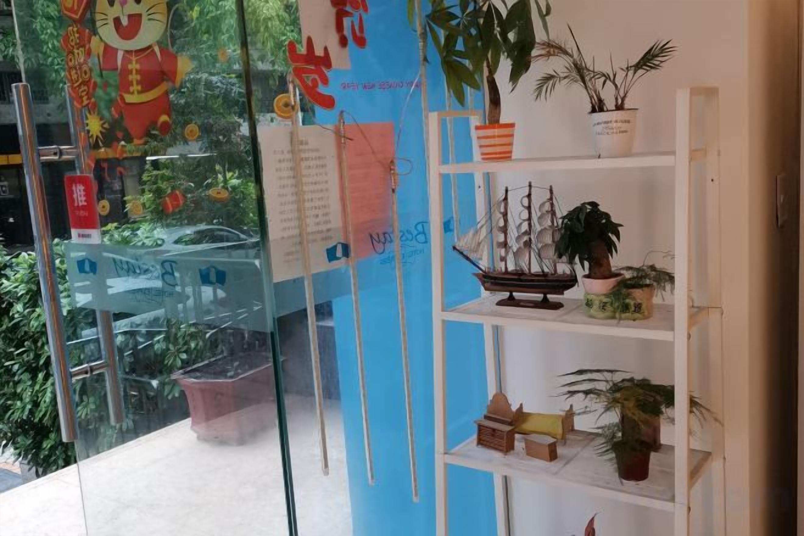Una habitación con pared de vidrio, estante con plantas en macetas y un pequeño modelo de barco.