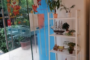 Una habitación con pared de vidrio, estante con plantas en macetas y un pequeño modelo de barco.