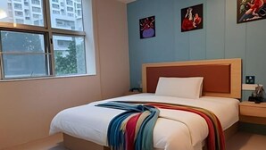 Un dormitorio con cama, mesita de noche, ventana y cuadros en la pared.