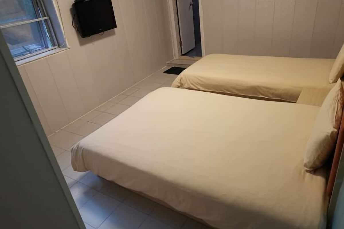 Quarto com duas camas, janela e televisão fixada na parede.