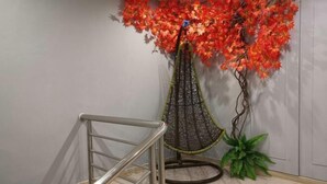 Una escalera con barandilla de metal, un sillón colgante decorativo con estructura de red, y un árbol artificial fijado a la pared con hojas rojas.