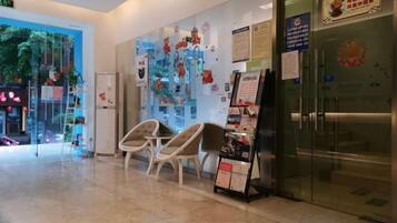 A reception area with a glass door, a seating area with chairs, and a wall with various posters and notices.