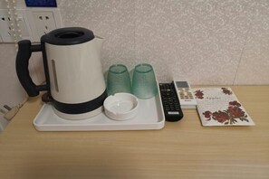 A coffee maker with a tray, two glass cups, a remote control, and a menu card on a wooden table. - Baishijie Hotel (Shantou)
