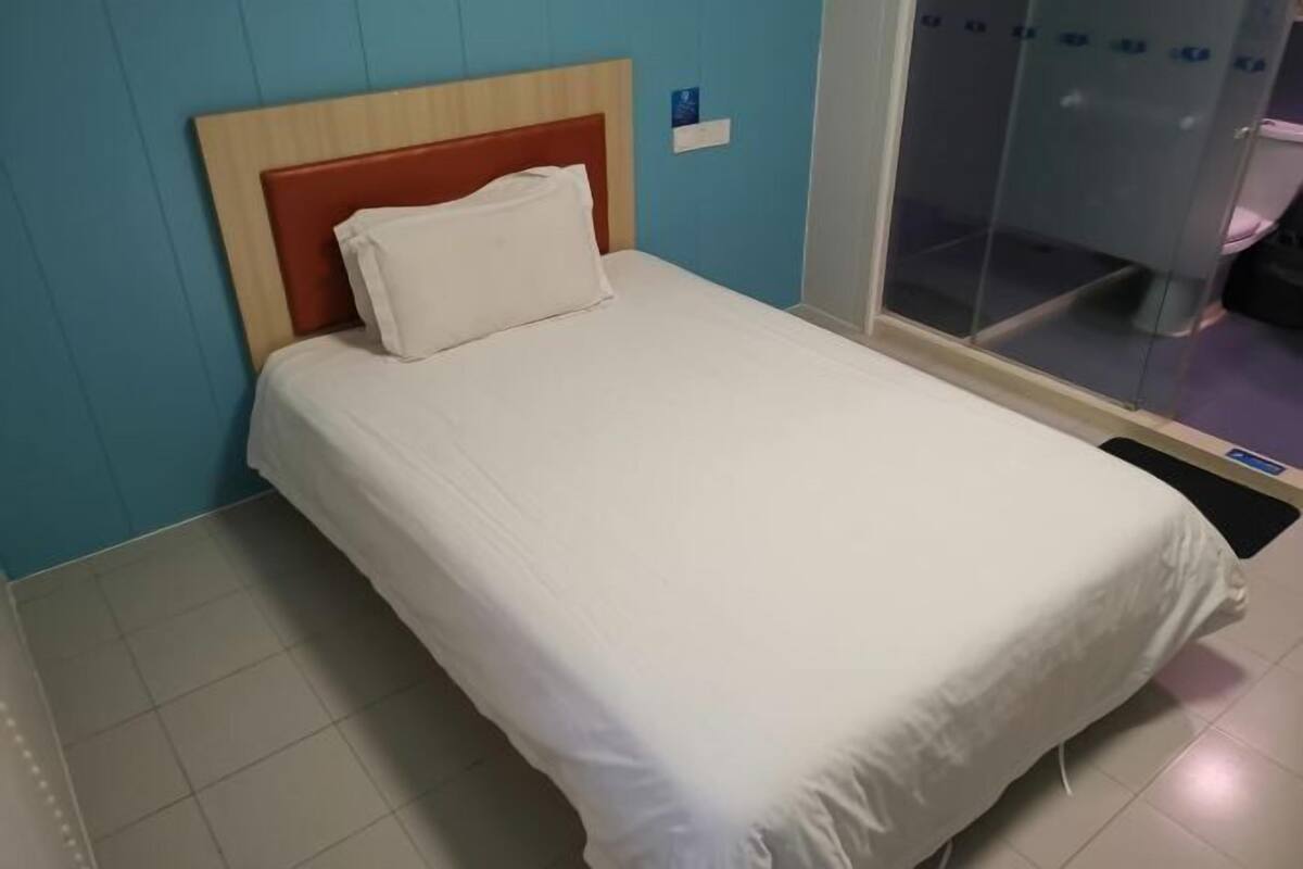 Cama de casal com cabeceira de madeira e roupa de cama branca em quarto com paredes azuis e divisória de vidro.