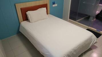 A single bed with a wooden headboard and white bedding in a room with blue walls and a glass partition.