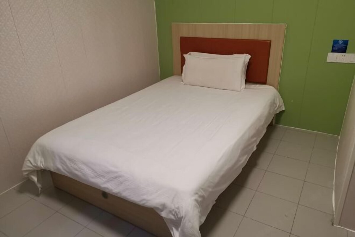 A single bed with a wooden frame and a white mattress, set against a green wall with a white headboard.