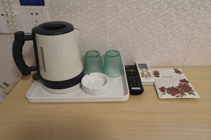 A coffee maker on a tray with two green cups and a small white cup, a remote control, and a menu card on a wooden table. - Baishijie Hotel (Shantou)