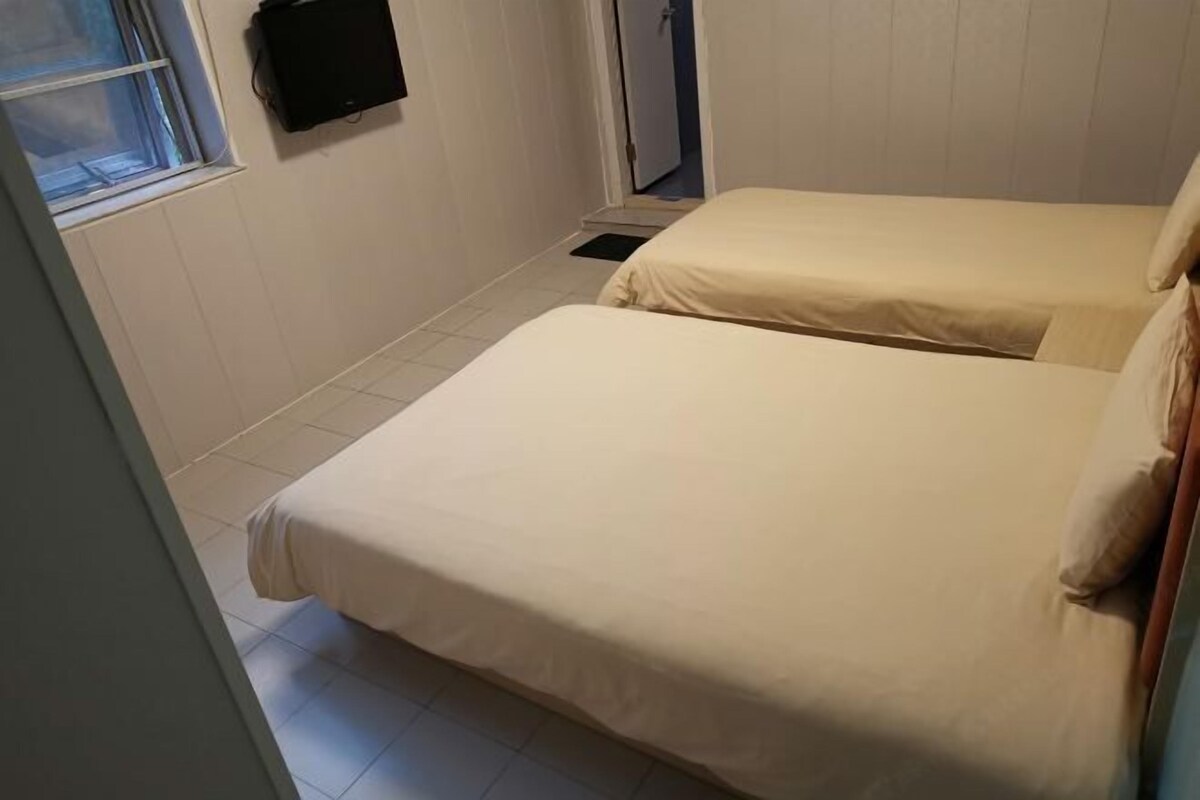 A room with two beds, a window, and a wall-mounted TV.
