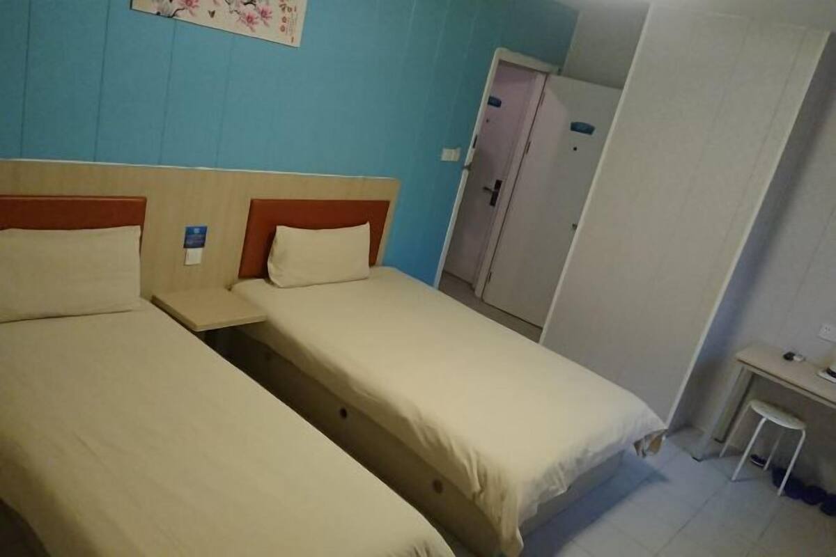 Quarto com duas camas de solteiro, uma escrivaninha e uma porta.