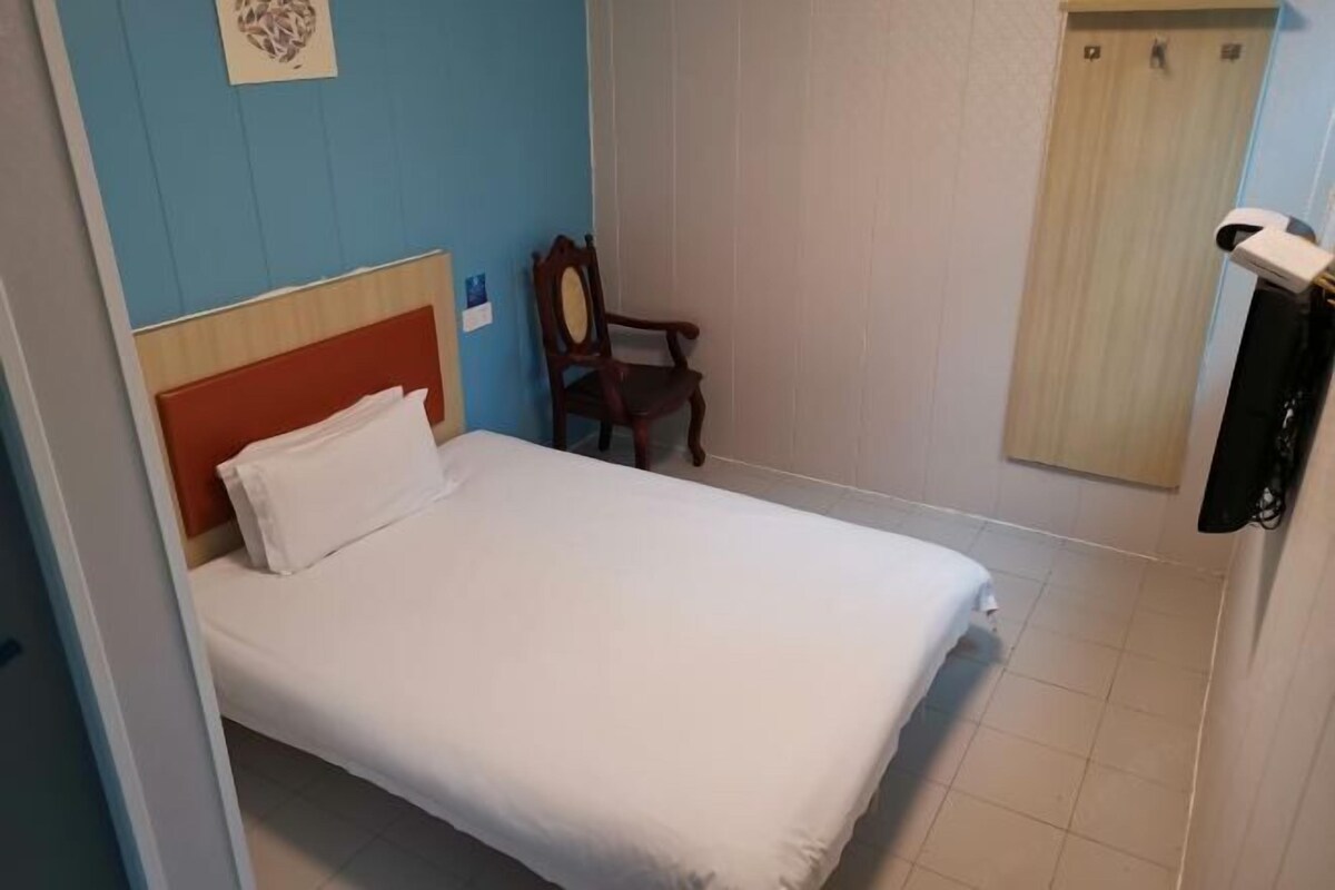 A single bed with a wooden headboard, a chair, a wall-mounted TV, and a curtain.