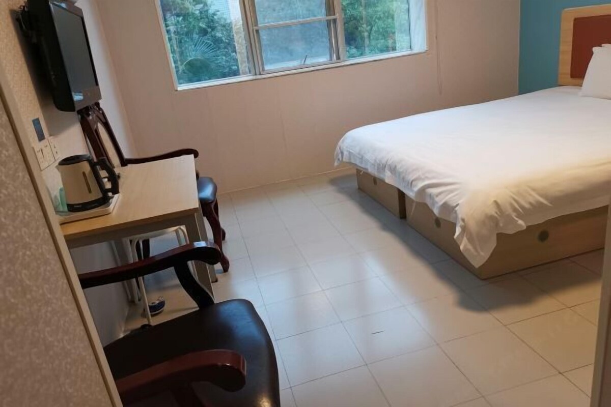 A bedroom with a bed, a desk, a chair, and a television on the wall.