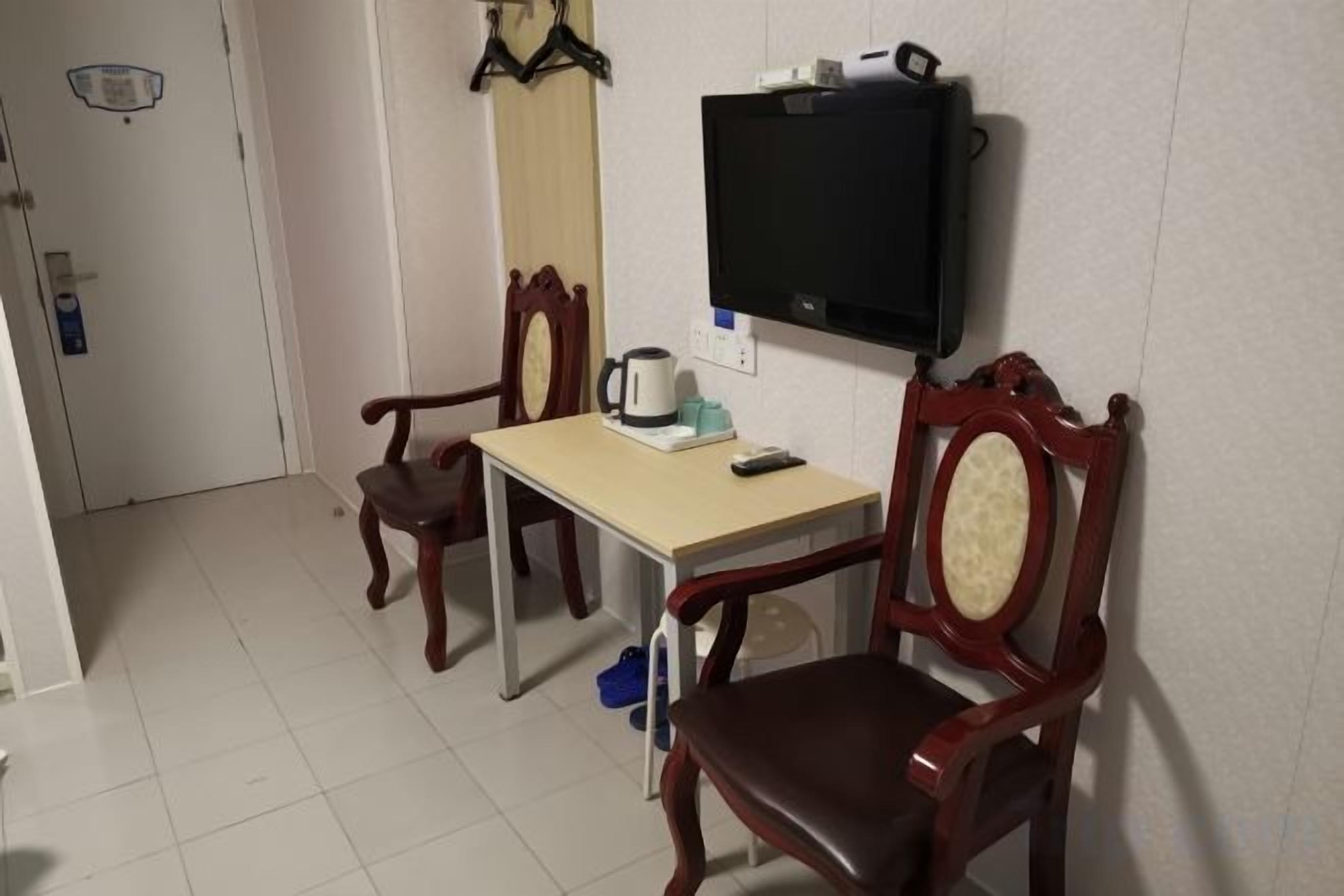 Una habitación pequeña y amoblada, con un televisor montado en la pared, una mesa con sillas y una puerta que da a otra habitación.