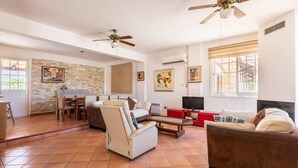 A spacious living room with a fireplace, a dining area, and a kitchen. There are ceiling fans, artwork on the walls, and large windows. - 4 Bedroom Villa With Private Pool Near Beach (Oroklini)